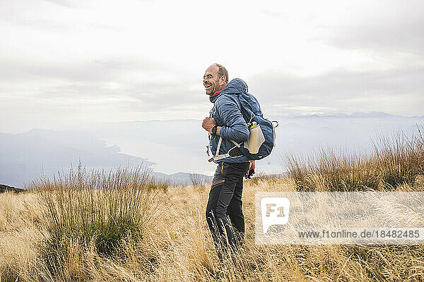 Happy mature man with backpack standing amidst grass