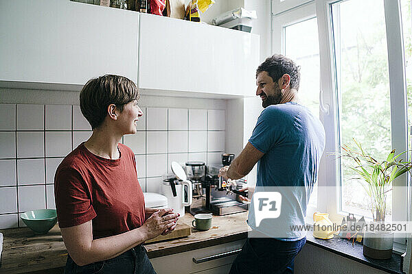 Frau spricht mit Mann  der zu Hause in der Küche Kaffee zubereitet