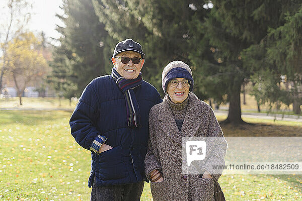 Smiling senior couple with hands in pockets standing at park