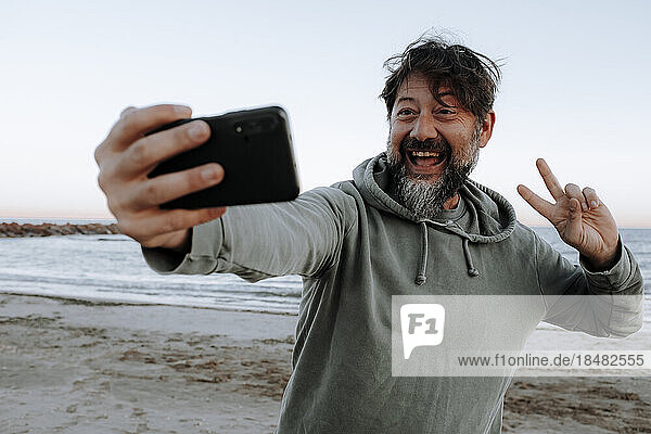 Glücklicher reifer Mann  der am Strand ein Selfie per Smartphone macht