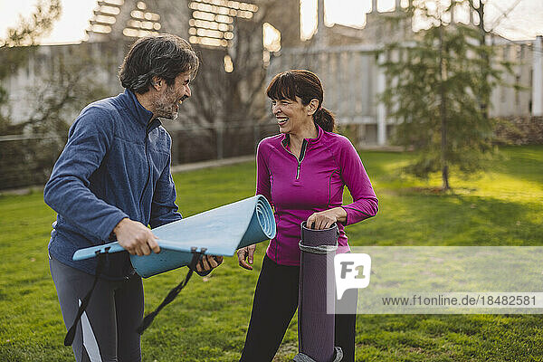 Happy mature man and woman with exercise mats in park