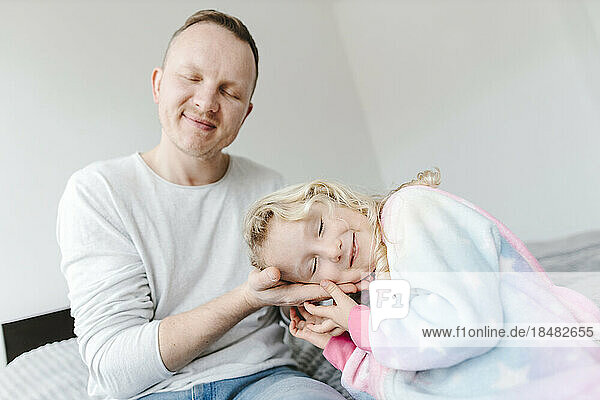 Smiling daughter leaning head on fathers hand at home