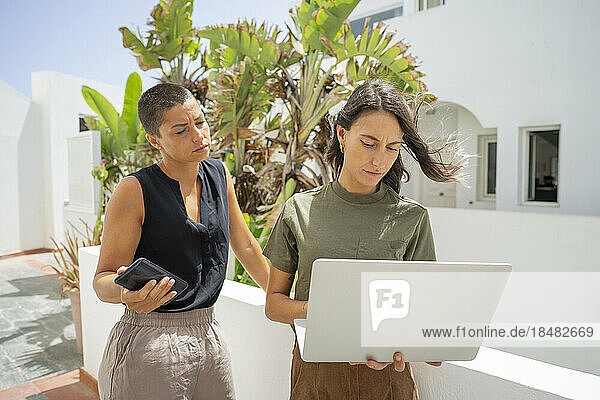Geschäftsfrau arbeitet am Laptop  während ein Kollege sein Smartphone in der Hand hält