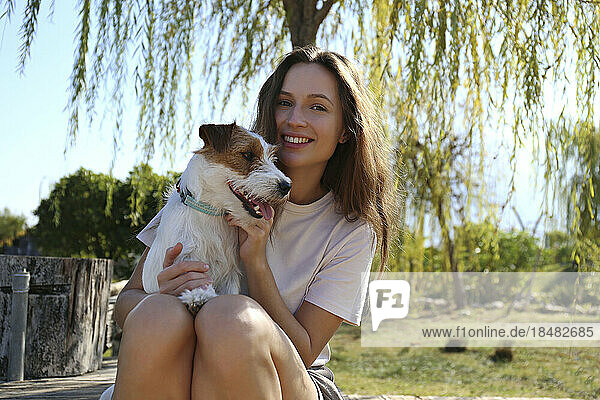 Happy young woman sitting with cute dog at park