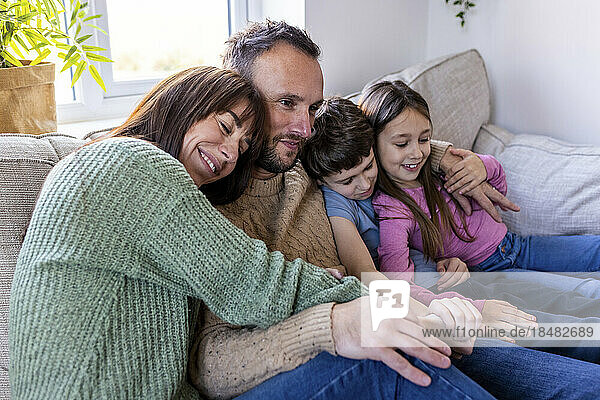 Smiling woman embracing family on sofa at home