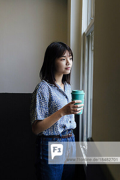 Businesswoman with reusable cup standing near window at office