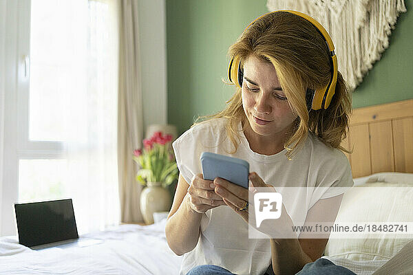 Smiling woman wearing wireless headphones using smart phone