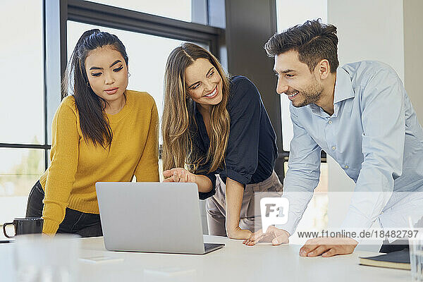 Happy businesswoman discussing with colleagues over laptop at workplace