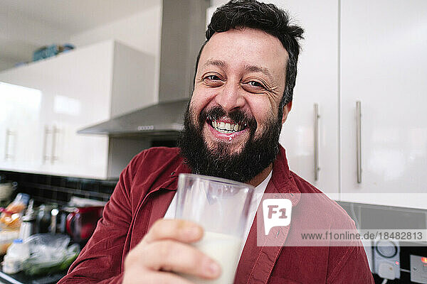 Happy man holding glass of milk in kitchen at home