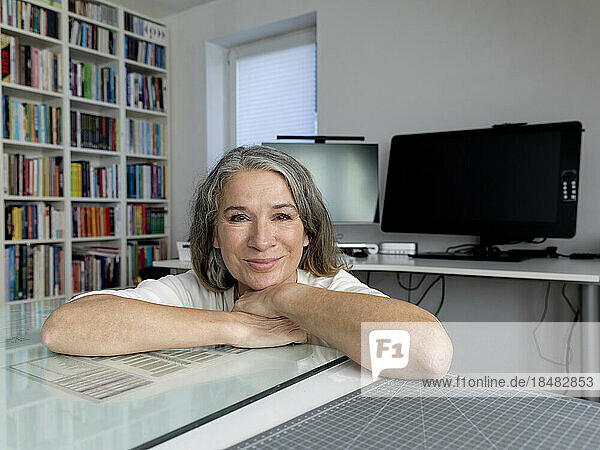 Smiling senior businesswoman leaning on desk in office