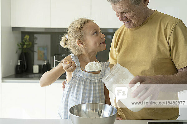 Grandfather looking at granddaughter holding flour in kitchen
