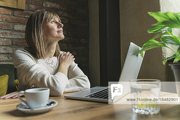 Contemplative freelancer with laptop sitting at table in cafe