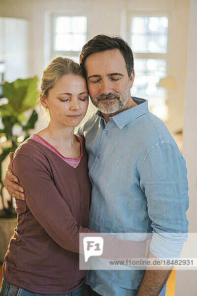 Woman embracing man with eyes closed standing at home