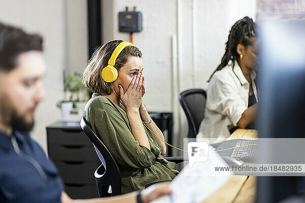 Businesswoman wearing headphones sitting in front of desktop at office