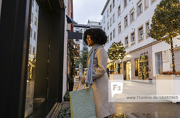 Happy young woman doing window shopping standing at footpath