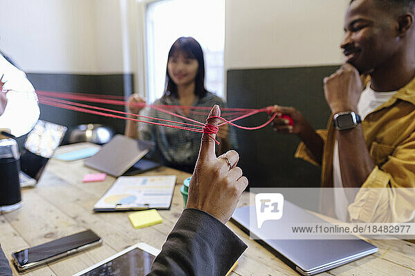 Hand of businesswoman playing cat's cradle with colleagues at office