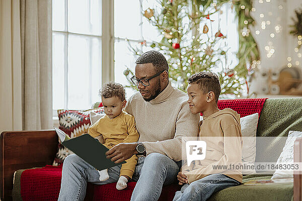 Father with daughter and son reading book on sofa at Christimas