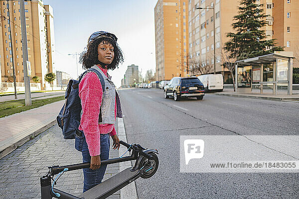 Lächelnde Frau mit Elektroroller steht auf der Straße