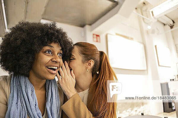 Überraschte Frau hört einer Freundin zu  die ihr ins Ohr flüstert