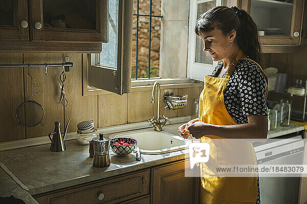 Young woman in yellow apron standing by kitchen counter