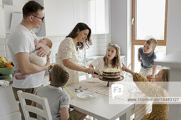 Mother cutting cake with children sitting at table in kitchen