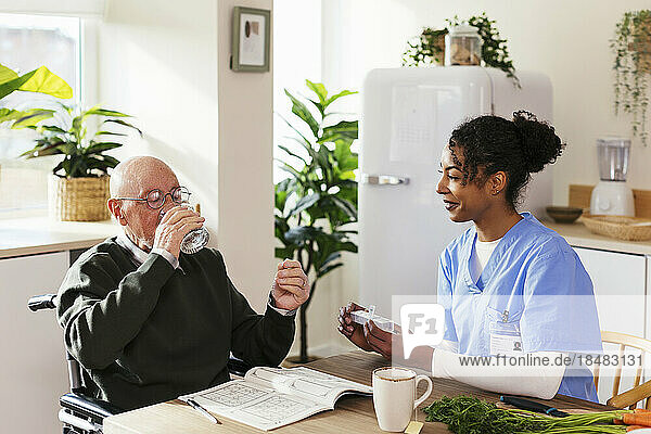 Nurse giving senior man's medicine at home