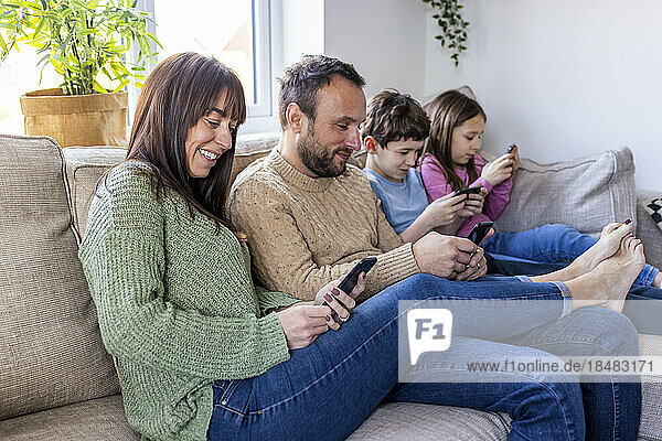 Happy man and woman with children using smart phone at home