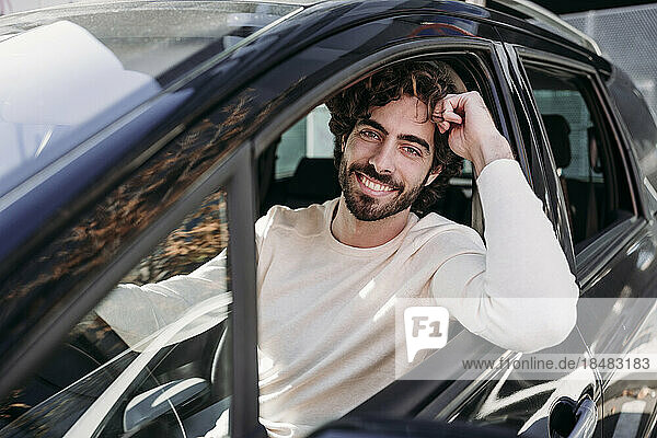 Lächelnder junger Mann mit Bart lehnt an Autofenster