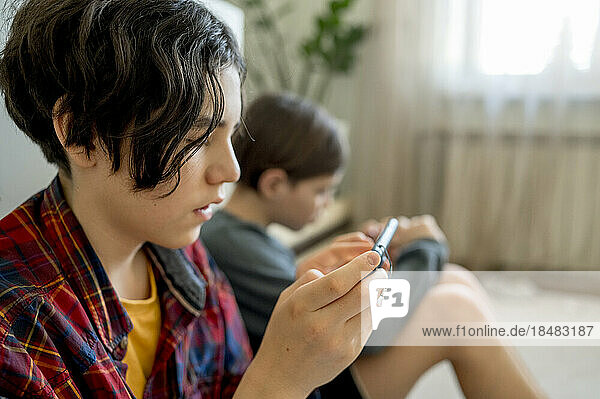 Boy playing video games on smart phone with brother sitting in background