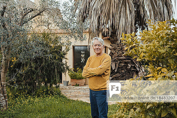 Smiling senior man standing with arms crossed in back yard