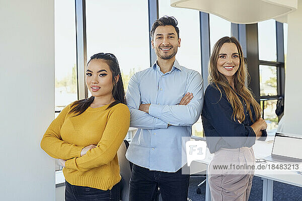 Confident business colleagues with arms crossed standing at workplace