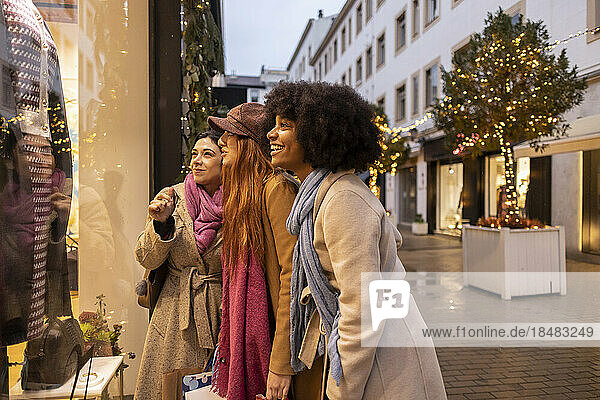 Happy young friends enjoying window shopping together in front of store