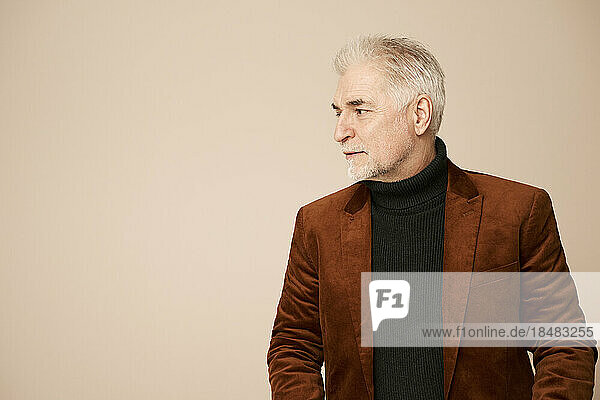 Handsome mature man wearing blazer against beige background