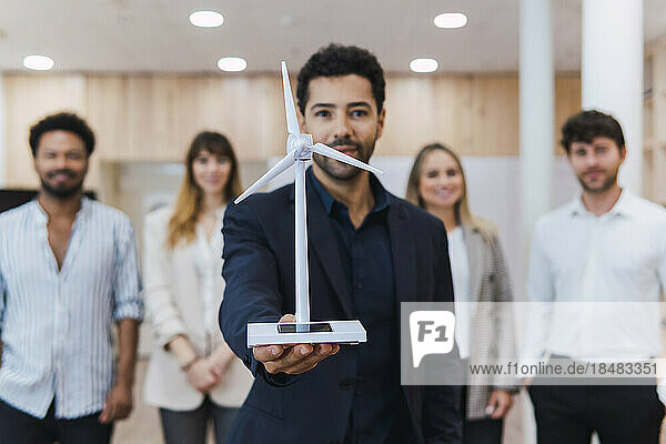 Businessman holding wind turbine model in front of his team in office