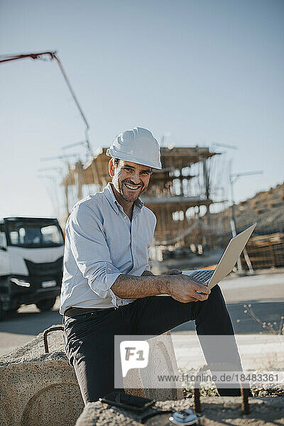 Happy mature architect with laptop at construction site