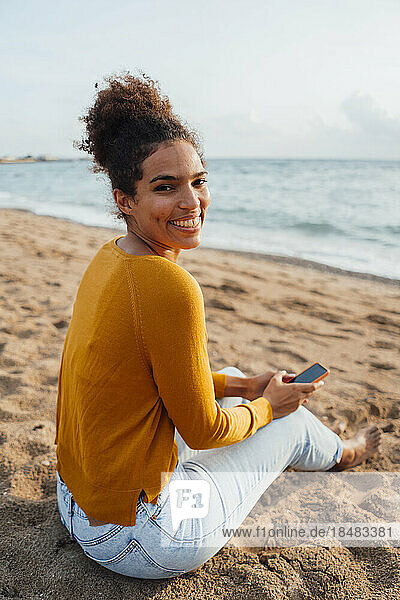 Happy young woman sitting with mobile phone at beach