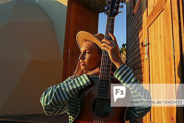 Thoughtful woman with guitar at sunset