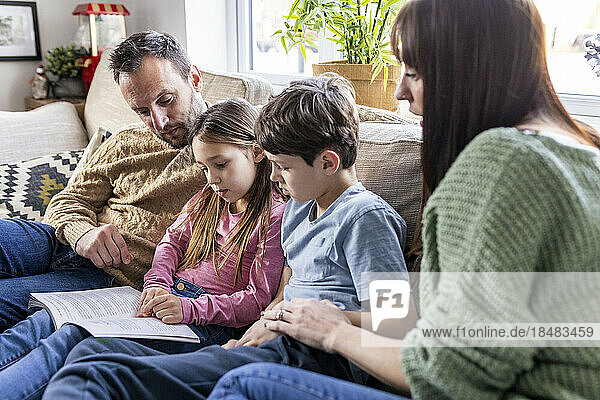 Girl reading book with family in living room at home