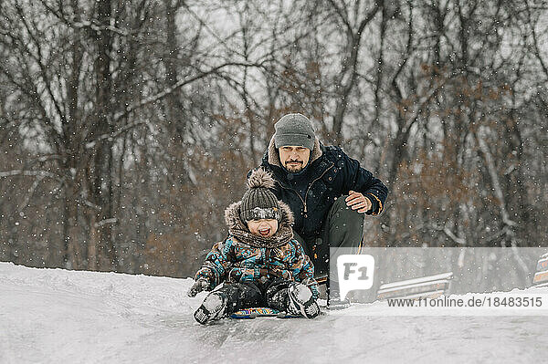 Vater und Sohn rodeln auf verschneitem Hügel hinunter