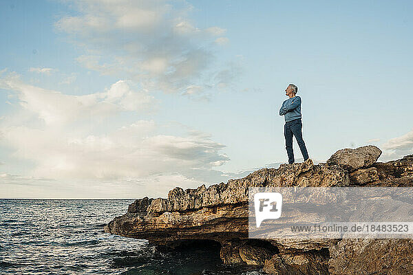 Senior man standing with arms crossed on rock