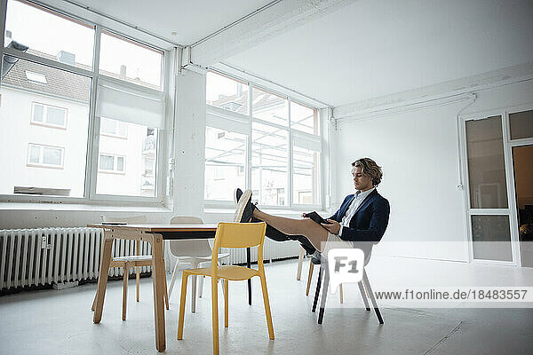 Junger Geschäftsmann sitzt mit Tablet-PC auf einem Stuhl im Büro