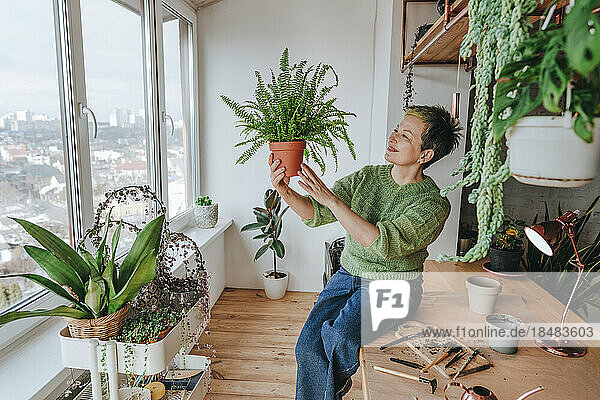 Smiling woman looking at fern plant at home