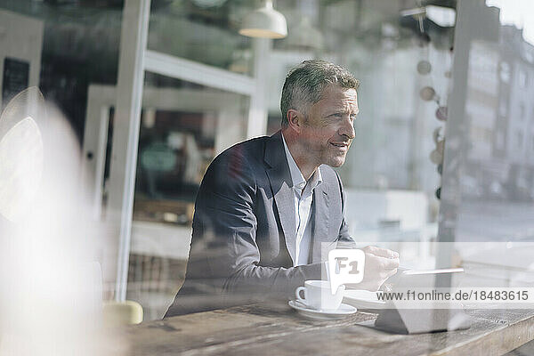 Mature businessman having breakfast seen through glass in cafe