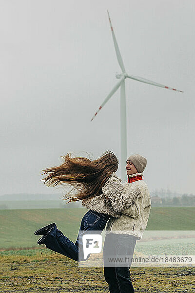 Happy teenage boyfriend spinning girlfriend in front of wind turbine