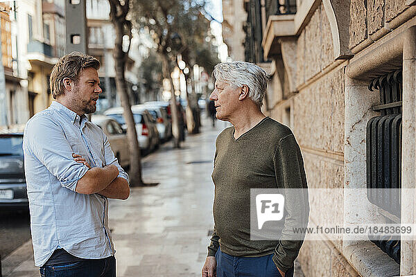 Mature man having discussion with father standing on footpath