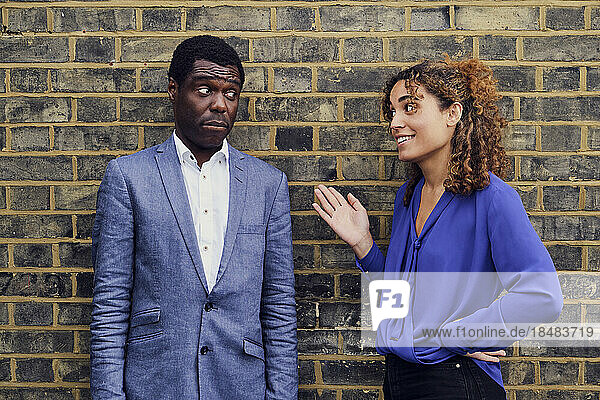 Smiling businesswoman gesturing and talking to colleague standing in front of brick wall