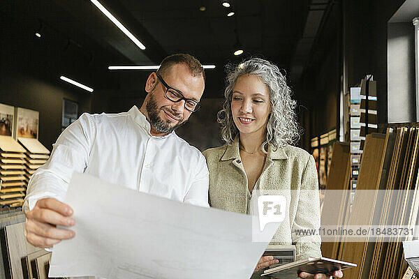 Two confident colleagues holding plan in architect's office