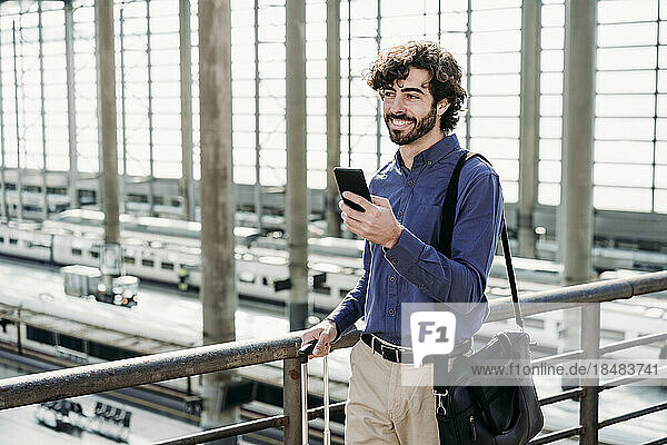Happy businessman with smart phone standing on bridge at station