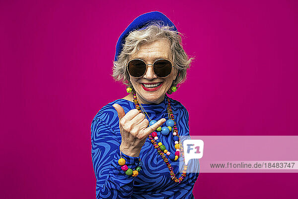 Cool senior woman gesturing against pink background
