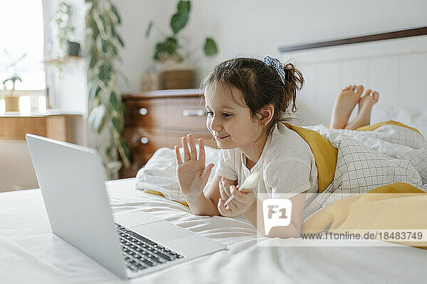 Lächelndes Mädchen winkt zu Hause per Videoanruf über den Laptop